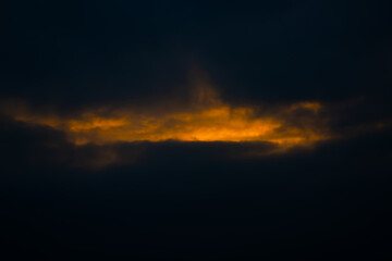 Dark fiery sunset fog with bright fiery sunlight shining through black clouds.
