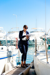 Female yachting dealer in marine blue suit holding notepad, standing outside a luxury sailboat,...