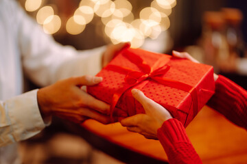 Exchange of gifts. Man gives to his woman surprise a gift box with red ribbon.Young loving couple celebrating Valentines Day. Romantic day. Winter holidays.