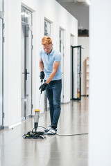 Young man works in the modern office. Uses vacuum cleaner