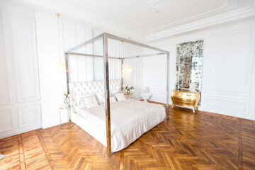 modern interior of a luxurious large bright bedroom. white stucco walls and a large four-poster bed and wooden parquet floor