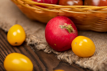 Green cucumbers, ripe radishes and colorful tomatoes in a wicker basket and scattered on the table. Close-up, selective focus.