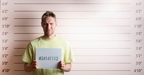 arrested prisoner young man holding a placecard in front of the height chart