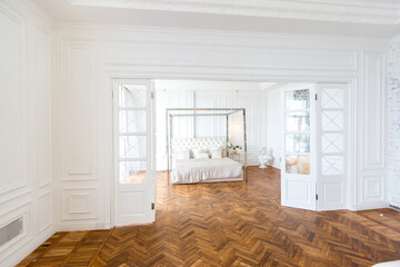 modern interior of a luxurious large bright bedroom. white stucco walls and a large four-poster bed and wooden parquet floor