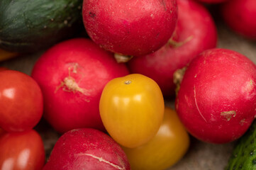 Green cucumbers, ripe radishes and colorful tomatoes scattered on the table. Close-up, selective focus.