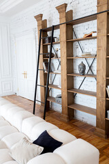 modern interior of a luxurious large bright living room. white expensive sofa and wooden shelving, white walls with moldings and a luxurious chandelier