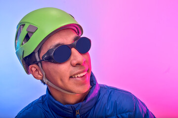 Young latin man smiling with green climbing helmet and blue jacket over colorful background