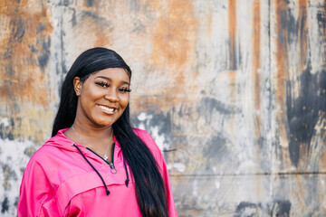 Smiling and happy beautiful African American teenage girl with long hair and a pink magenta jacket standing  outside in an urban city setting © Ursula Page