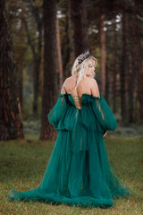 Naklejka premium young beautiful blonde hair woman queen. Princess walks. autumn green forest mystic. Vintage medieval shiny crown. Long evening green dress. magic fantasy. back view