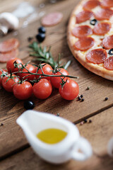 Ripe cherry tomatoes lie on a brown wooden table. Next to the ingredients for making pizza: dough, butter, flour and mushrooms. Natural light. Rustic style
