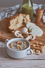 Close-up of mushroom cream puree soup on a white table. Next around the ingredients: mushrooms, onions, crackers, bread, milk and butter. Rustic style