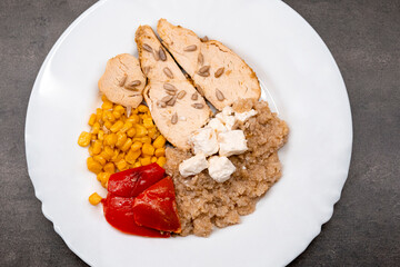 Chicken salad, grilled corn, quinoi, roasted peppers and feta. Healthy food served on a white plate. Dark background