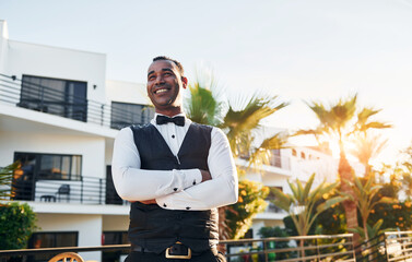 Posing for a camera. Black waiter in formal clothes is at his work outdoors at sunny daytime