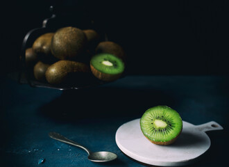kiwi cut in the foreground on a white cutting board, in the background iron bowl with other kiwis,...