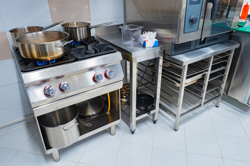 Industrial gas stove in a restaurant. Chrome gas stove. Concept - restaurant equipment. Sale of restaurant equipment. Something is being prepared in cafe kitchen. Pans on a gas stove