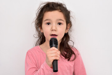 Happy cute little girl singing a song on a microphone. Emotional portrait of a happy child. She has...