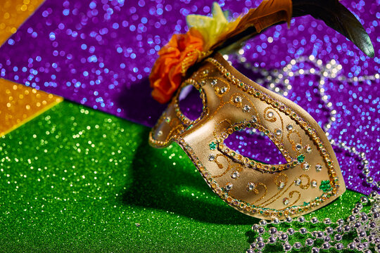 Festive, colorful Mardi Gras or carnivale mask and beads on golden, green and purple background. Venetian masks. Party invitation, greeting card, venetian carnivale celebration concept.