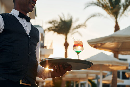 Close up view of drink. Black waiter in formal clothes is at his work outdoors at sunny daytime