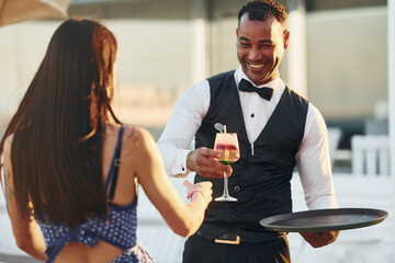 Order for woman. Black waiter in formal clothes is at his work outdoors at sunny daytime