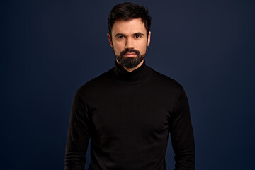 Fototapeta premium Confident good-looking male entrepreneur in black high neck sweater, smirk and self-assured, standing assertive. Handsome macho man