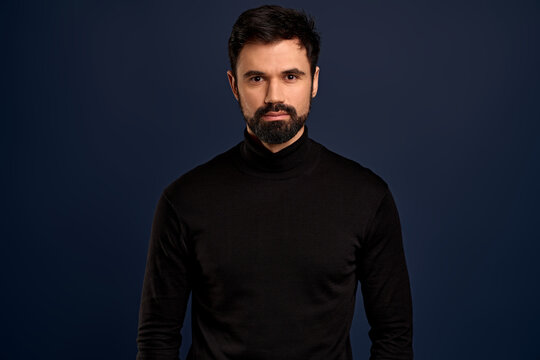 Confident good-looking male entrepreneur in black high neck sweater, smirk and self-assured, standing assertive. Handsome macho man
