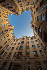 Bottom-up view from a rectangular courtyard surrounded by multi-storey buildings. The blue sky above the courtyard is crossed by wire. European city. No people