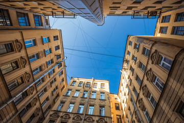 Bottom-up view from a non-rectangular courtyard surrounded by multi-storey buildings. The blue sky above the courtyard is lined with intersecting wires. European city. No people