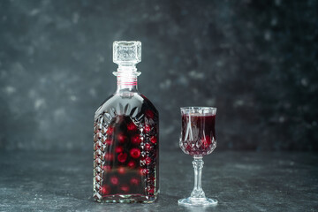 Homemade tincture of red cherry in a glass bottle and a wine crystal glass , Ukraine, close up