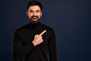 Cheerful, excited young bearded guy in high neck sweater, pointing upper right corner, hear great news, suggest visit event see yourself, recommend awesome store, stand Pacific Blue background