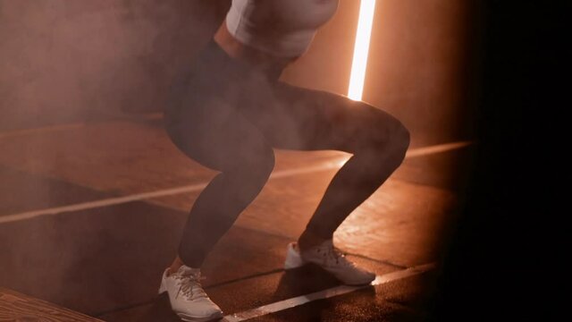 fit young woman in white top and black leggings in a crossfit box in a close up doing squats in a moody lighting