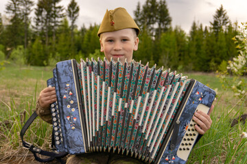 A boy in a military uniform holds an accordion in his hands. Victory Day. 9th May. A Great Victory.
