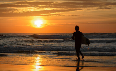 silhouette surfer person running on the beach at sunset