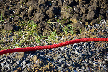 Red flexible double-walled pipe for cable ducts. Corrugated plastic pipe is buried in the ground...