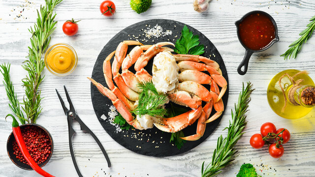 Boiled crab claws on a black stone plate. On a white wooden background. Rustic style.