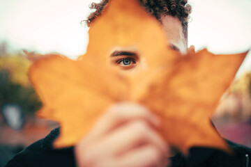 Young man looking through hole on maple leaf