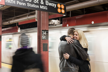 Girlfriend smiling while embracing boyfriend standing at subway station
