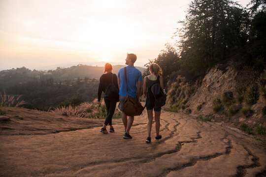 Friends with bag walking together on mountain path during sunset