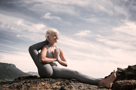 Smiling flexible woman with eyes closed practicing Eka Pada Sirsasana at beach against sky