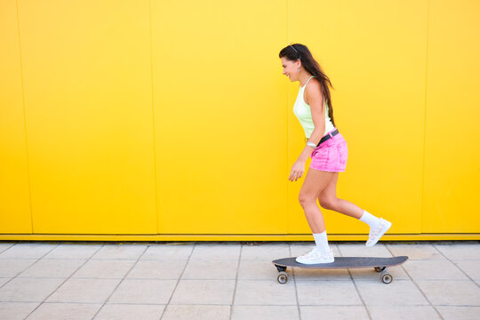 Beautiful girl skateboarding along yellow wall in summer