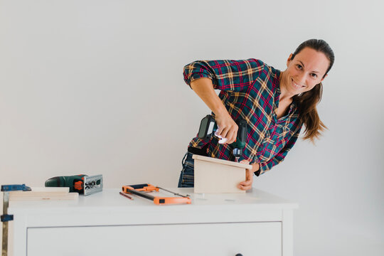 Smiling woman doing DIY work while standing against wall at home