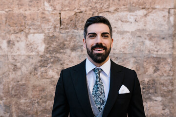 Happy groom with suit and necktie against wall