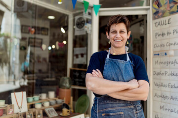 Happy small business owner standing with arms crossed outside her store