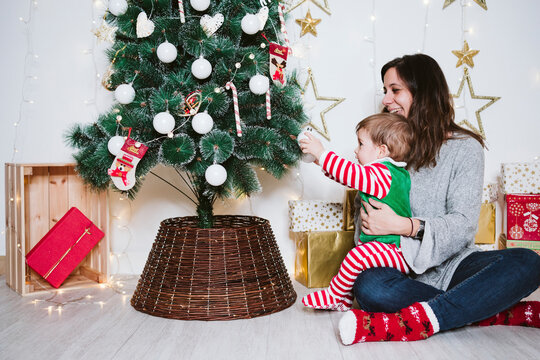 Smiling mother and son playing with bauble on Christmas tree while sitting at home