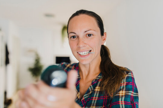 Mid adult woman holding screw in mouth while working with electric screwdriver at home