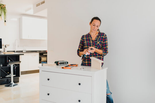 Woman changing drill bit while standing by cabinet at home