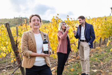Female entrepreneur holding wine bottle while clients standing and drinking during autumn