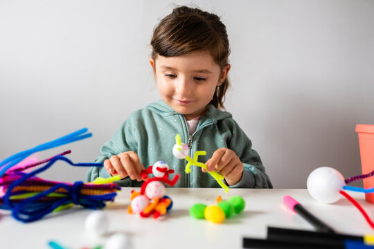 Smiling girl playing with pipe cleaners and pom-pom toys against wall