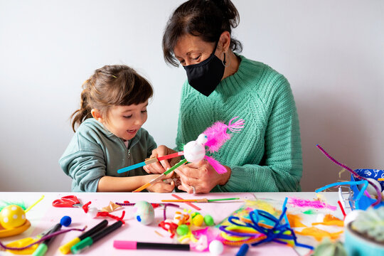 Grandmother and granddaughter making creative toys from pipe cleaners and pom-pom during COVID-19