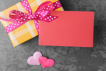 Red blank card on yellow gift box over grey stone background. Valentine’s day greeting
