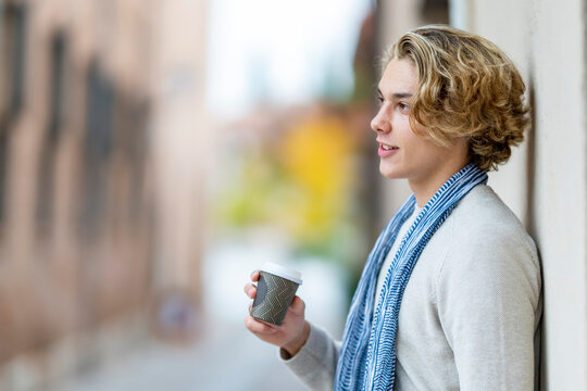 Young man drinking coffee while leaning on wall